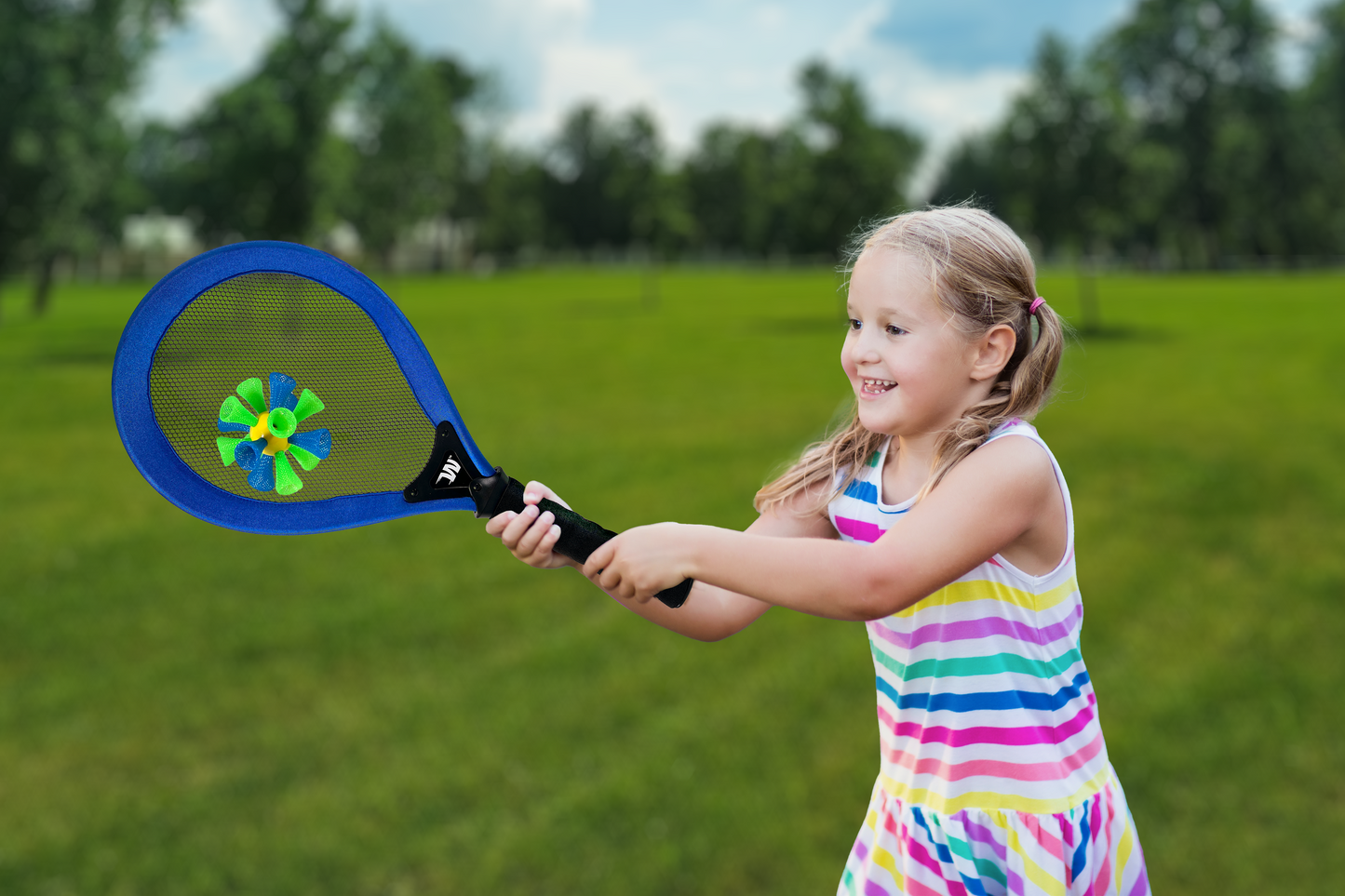 Child holding a racket about to hit a birdie ball in a grassy outdoor setting