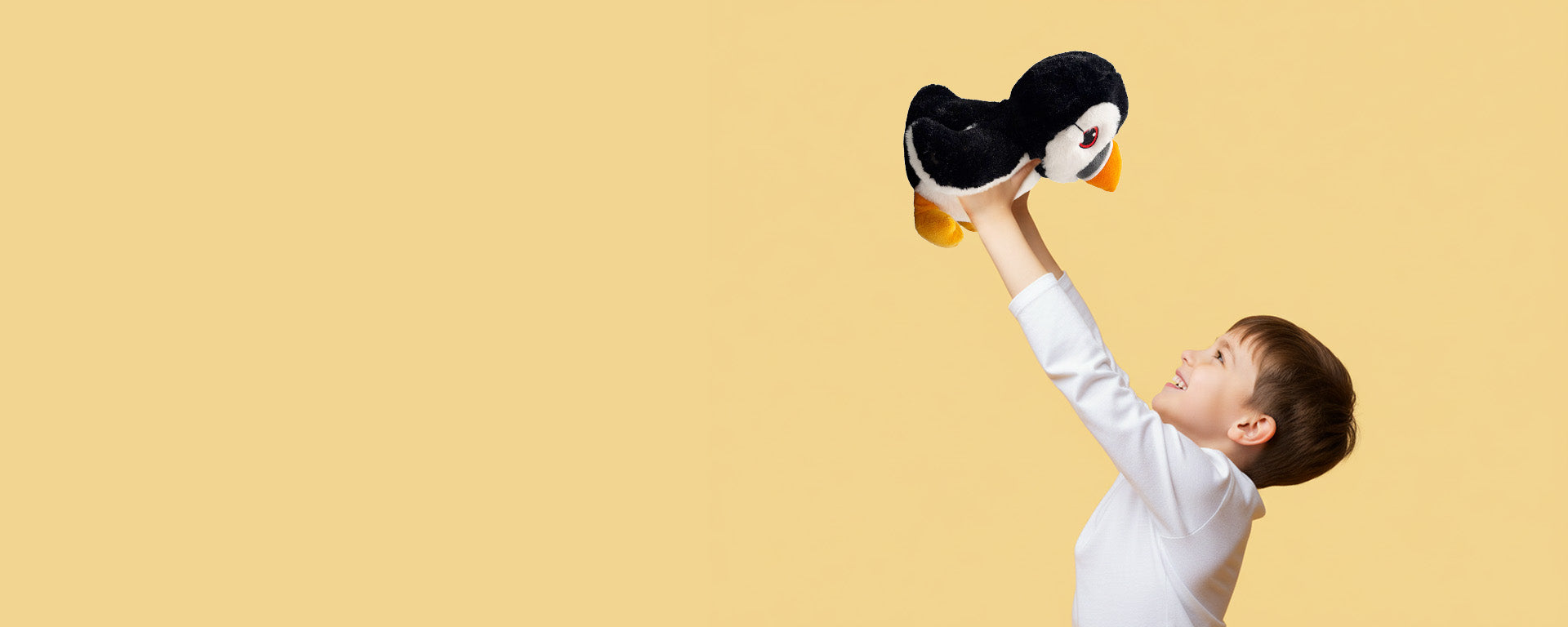 Child holding a puffin plush toy against a beige background